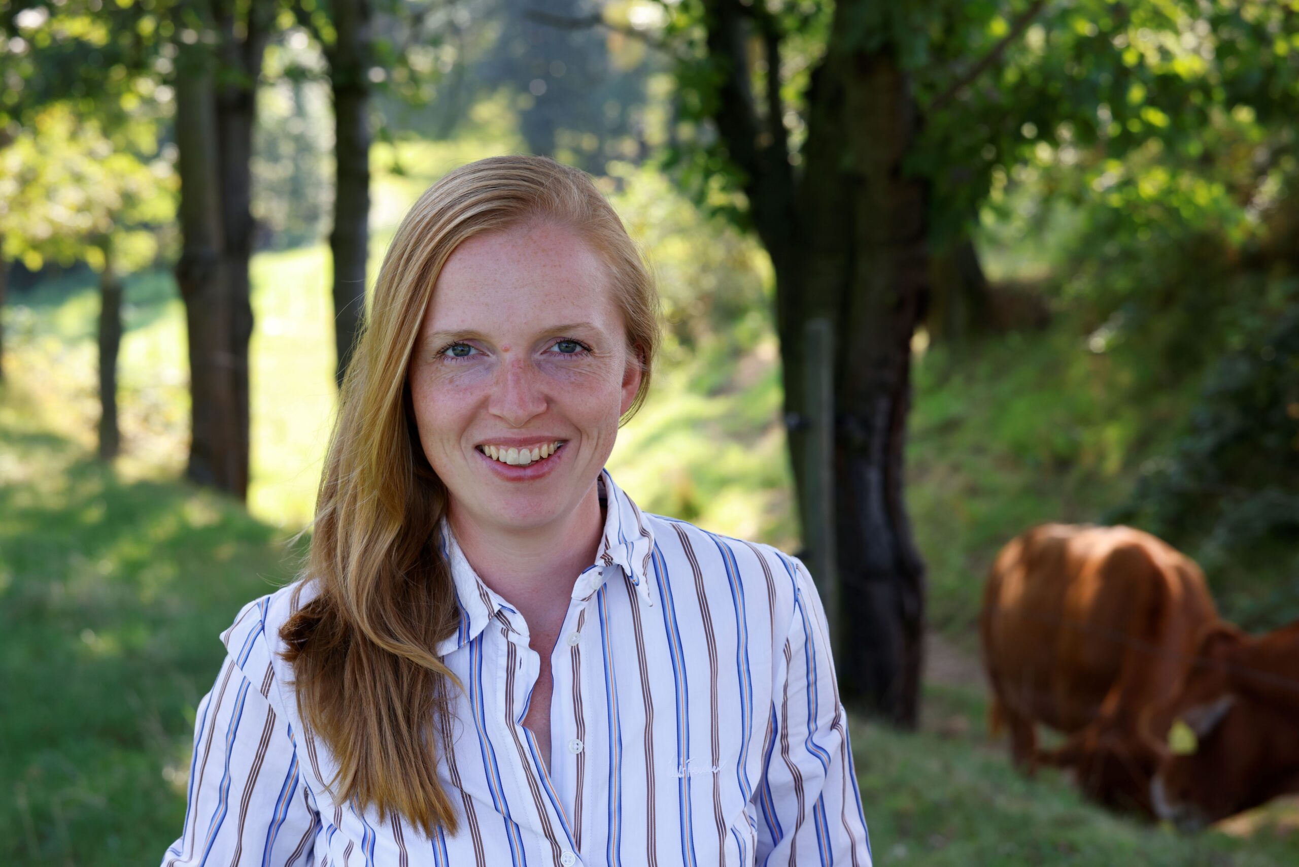 Landwirtin lächelt vor Bäumen und ihren Tieren, verbunden mit ihnen